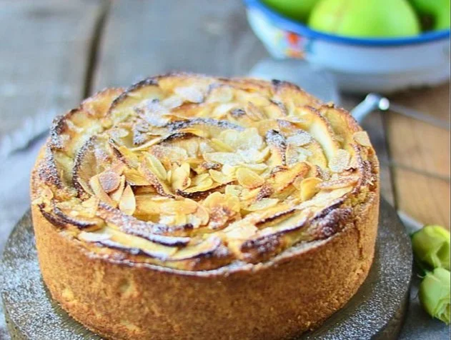 Apfel Mazarin Kuchen auf einem Teller, mit frischen Äpfeln und Mandelblättchen garniert.