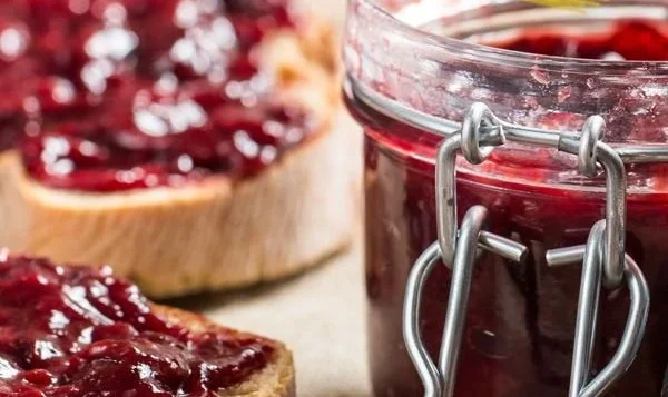 Ein Glas selbstgemachte Marmelade auf einem Holztisch mit frischen Früchten.