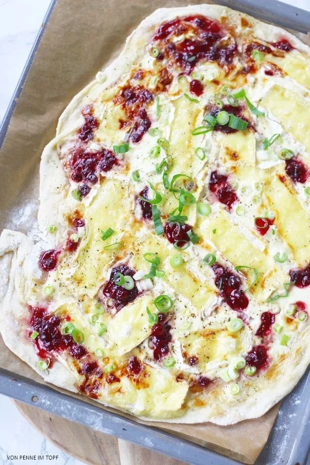 Flammkuchen mit Camembert und Preiselbeeren auf einem Holzbrett