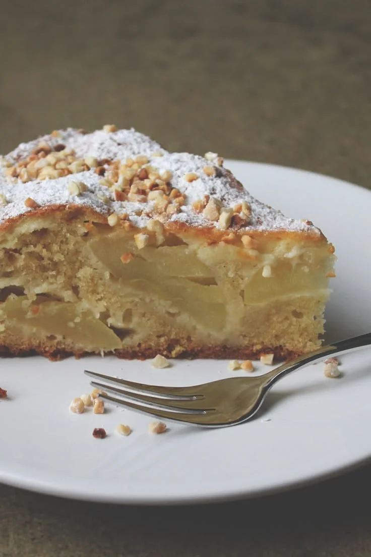 Französischer Apfelkuchen mit Crème fraîche und Mandeln auf einem weißen Teller
