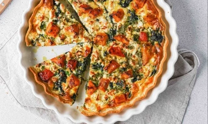Quiche mit Kürbis, Feta und Spinat auf einem Teller serviert