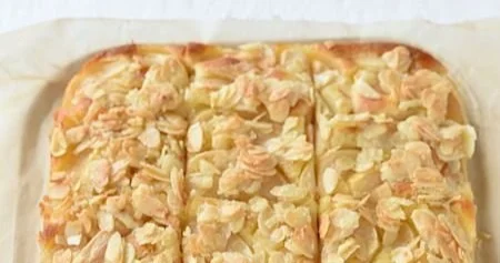 Saftiger Apfelkuchen mit Mandelkruste auf einem Teller, dekoriert mit frischen Äpfeln.