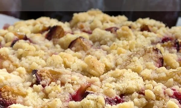 Saftiger Pflaumen-Streusel-Kuchen auf einem Teller mit frischen Pflaumen